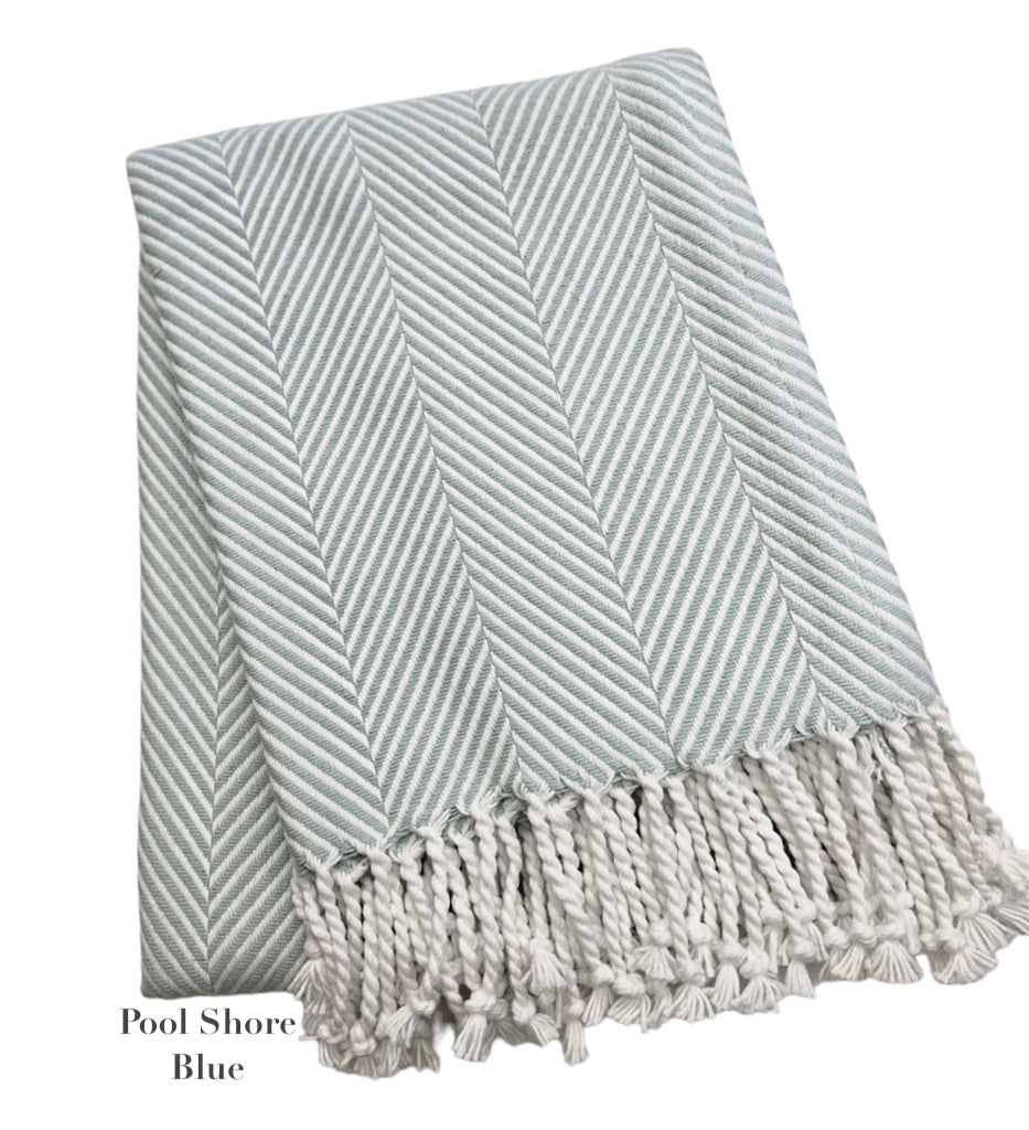 A folded light blue and white throw from the Nantucket Herringbone Throw Collection by A Soft Idea, featuring hand knotted fringe, labeled "Pool Shore Blue.