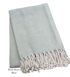 A folded light blue and white throw from the Nantucket Herringbone Throw Collection by A Soft Idea, featuring hand knotted fringe, labeled "Pool Shore Blue.
