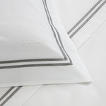 Experience luxury with Frette's Classic White/Grey Bedding Collection—100% cotton pillowcase and sheet set featuring a grey double-line border and an embroidered "FRETTE" for a timeless, elegant touch.