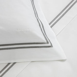Experience luxury with Frette's Classic White/Grey Bedding Collection—100% cotton pillowcase and sheet set featuring a grey double-line border and an embroidered "FRETTE" for a timeless, elegant touch.