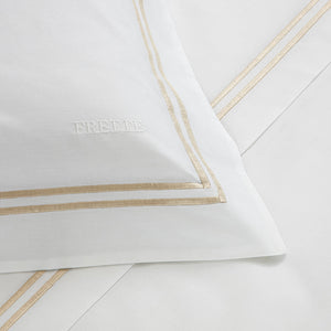 The Classic White/Khaki Bedding Collection by Frette features a luxurious 100% cotton sheet set with beige double-line borders and the brand name "Frette" embroidered on the pillowcase.