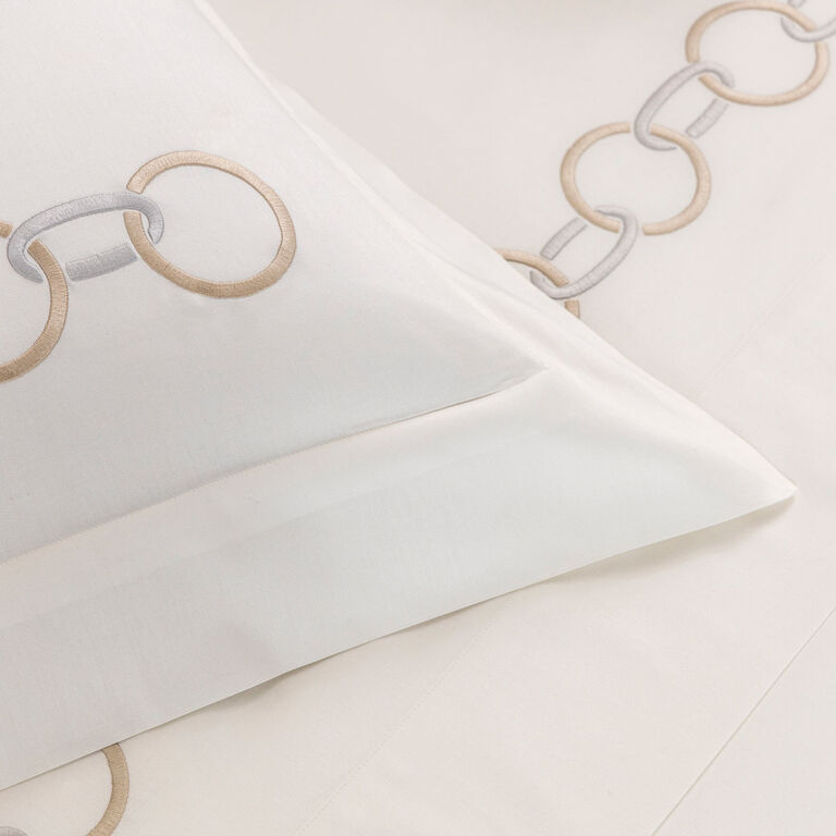 Close-up of a white cotton sateen sheet from Frette's Links Embroidery Bedding Collection, featuring elegant beige and gray chain embroidery along the edges.