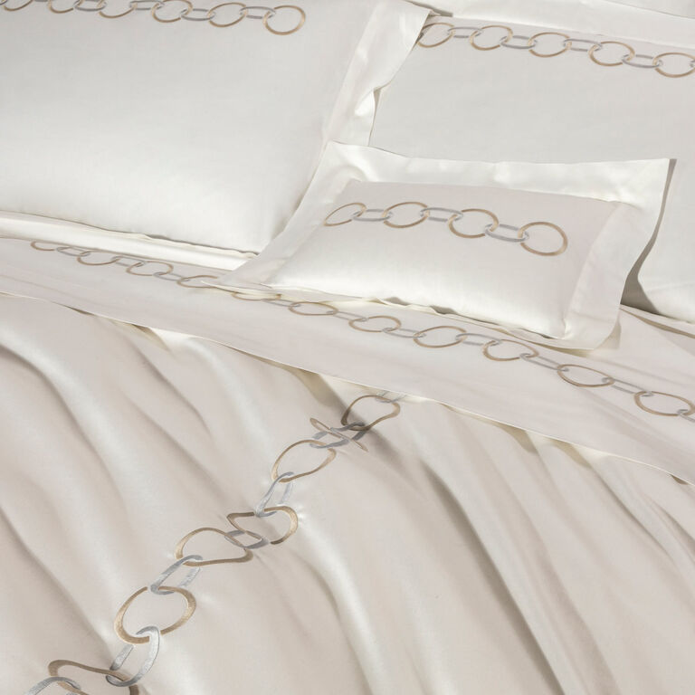 The Links Embroidery Bedding Collection by Frette features white cotton sateen sheets with elegant beige and gray chain ring embroidery along the edges of the pillowcases, sheet, and duvet cover.