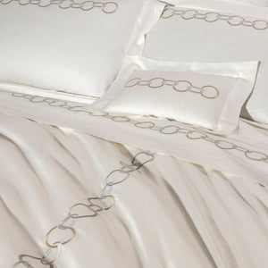 The Links Embroidery Bedding Collection by Frette features white cotton sateen sheets with elegant beige and gray chain ring embroidery along the edges of the pillowcases, sheet, and duvet cover.
