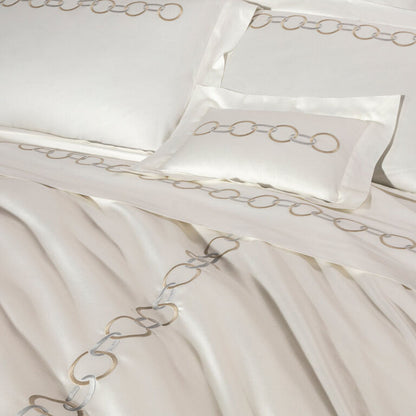 The Links Embroidery Bedding Collection by Frette features white cotton sateen sheets with elegant beige and gray chain ring embroidery along the edges of the pillowcases, sheet, and duvet cover.