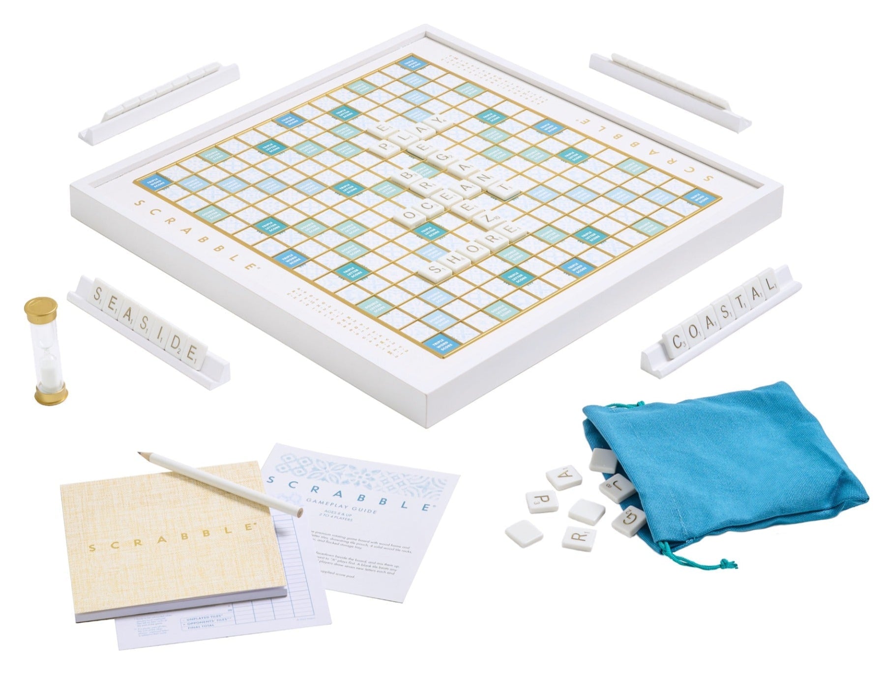 The WS Game Company's Scrabble Bianco Edition includes a wood-framed board, tiles, racks spelling "SEASIDE" and "COASTAL," plus a scorepad, hourglass timer, and a blue tile bag with an ocean breeze design.