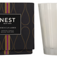 A Nest Moroccan Amber Candle Collection box sits next to a clear glass candle, filling the air with warm notes of patchouli and bergamot.