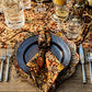 A formal table setting with floral-patterned plates featuring an elegant floral motif, the Willa Amber Napkin Set by Juliska, silver cutlery, glassware, and a decorative tablecloth.