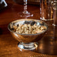 The Juliska Graham Cocktail Bowl, crafted from hammered stainless steel, is filled with pistachios and rests on a polished wooden table—an elegant choice for showcasing snacks at your next cocktail hour.