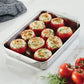 The Hestan Provisions OvenBond Tri-ply Rectangular Baker, shown on a white countertop with fresh tomatoes and a gray cloth, holds nine baked stuffed tomatoes topped with herbs—ideal for holiday entertaining.