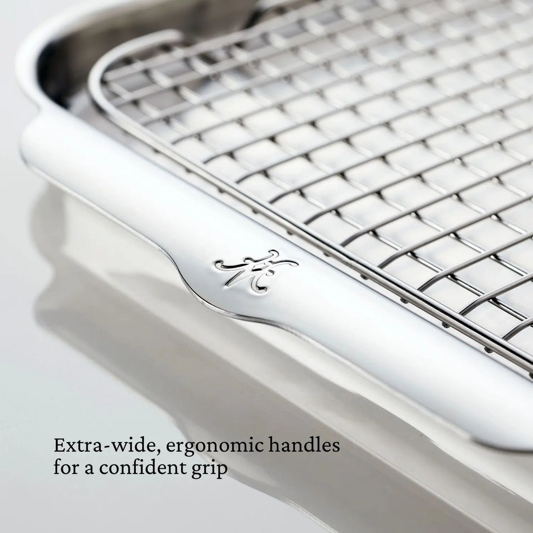 Close-up of the Hestan Provisions OvenBond Tri-ply 3-Piece Set rack with warp-resistant, extra-wide ergonomic handles and decorative logo on a reflective surface. Text: "Confident grip—perfect for your Half Sheet Pan.