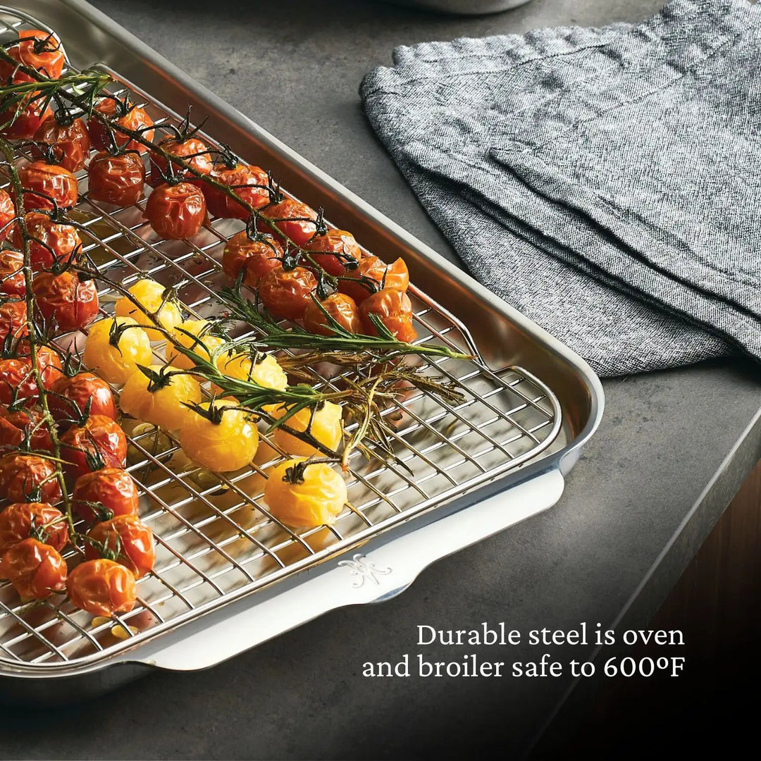 Roasted red and yellow tomatoes with herbs rest on the Hestan Provisions OvenBond Tri-ply 3-Piece Set’s warp-resistant pan and wire rack. A stack of gray kitchen towels sits nearby. This stainless steel set is oven and broiler safe to 600°F.