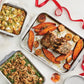 A roasted rack of pork with sweet potatoes, onions, green bean casserole, and herbed stuffing is artfully arranged on a Hestan Provisions OvenBond Tri-ply 5-Piece Set pan, set atop a white table adorned with a red ribbon.