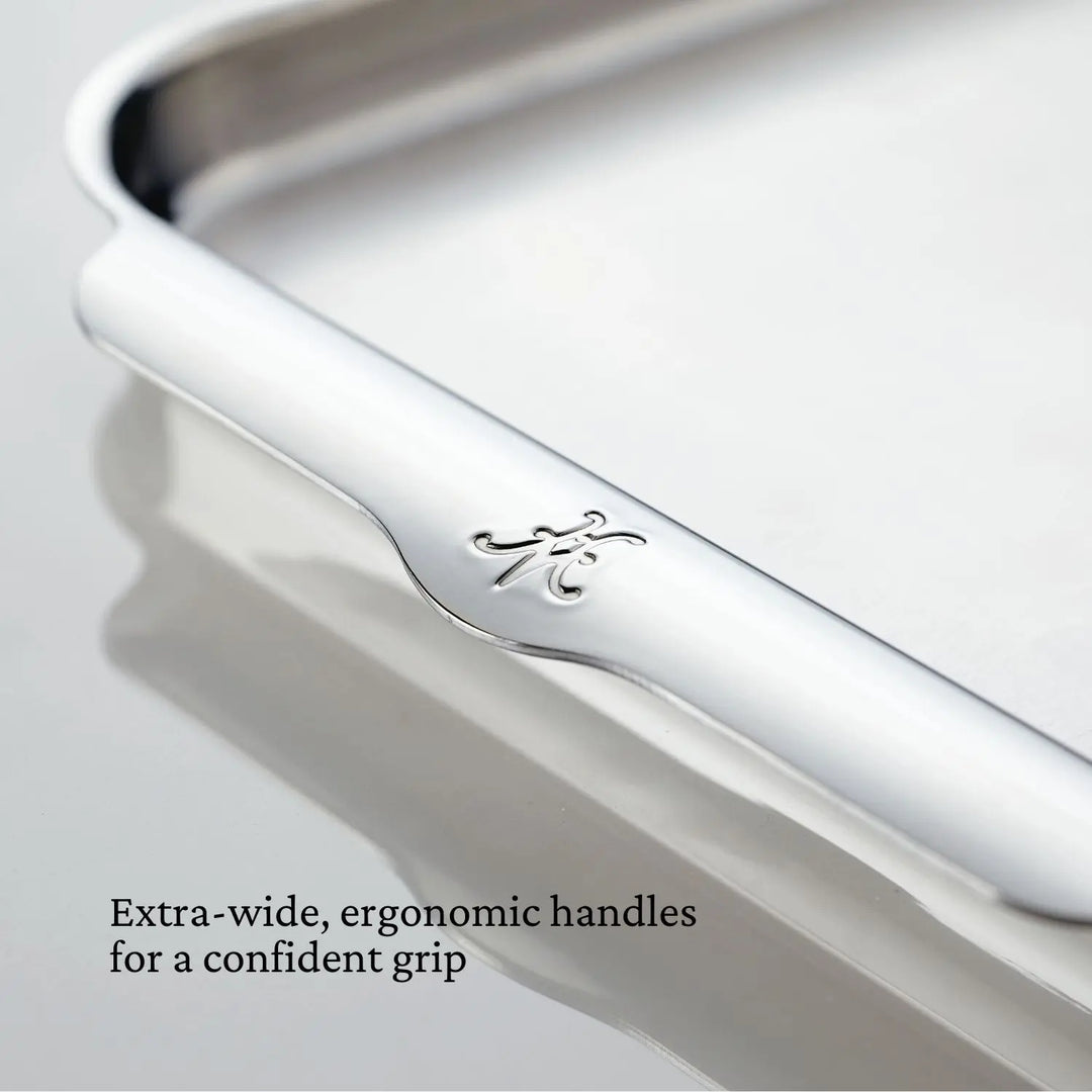 Close-up of a Hestan Provisions OvenBond Sheet Pan Collection tray with engraved monogram and extra-wide handles; text: “Extra-wide, ergonomic handles for a confident grip.” Oven safe to 600°F.