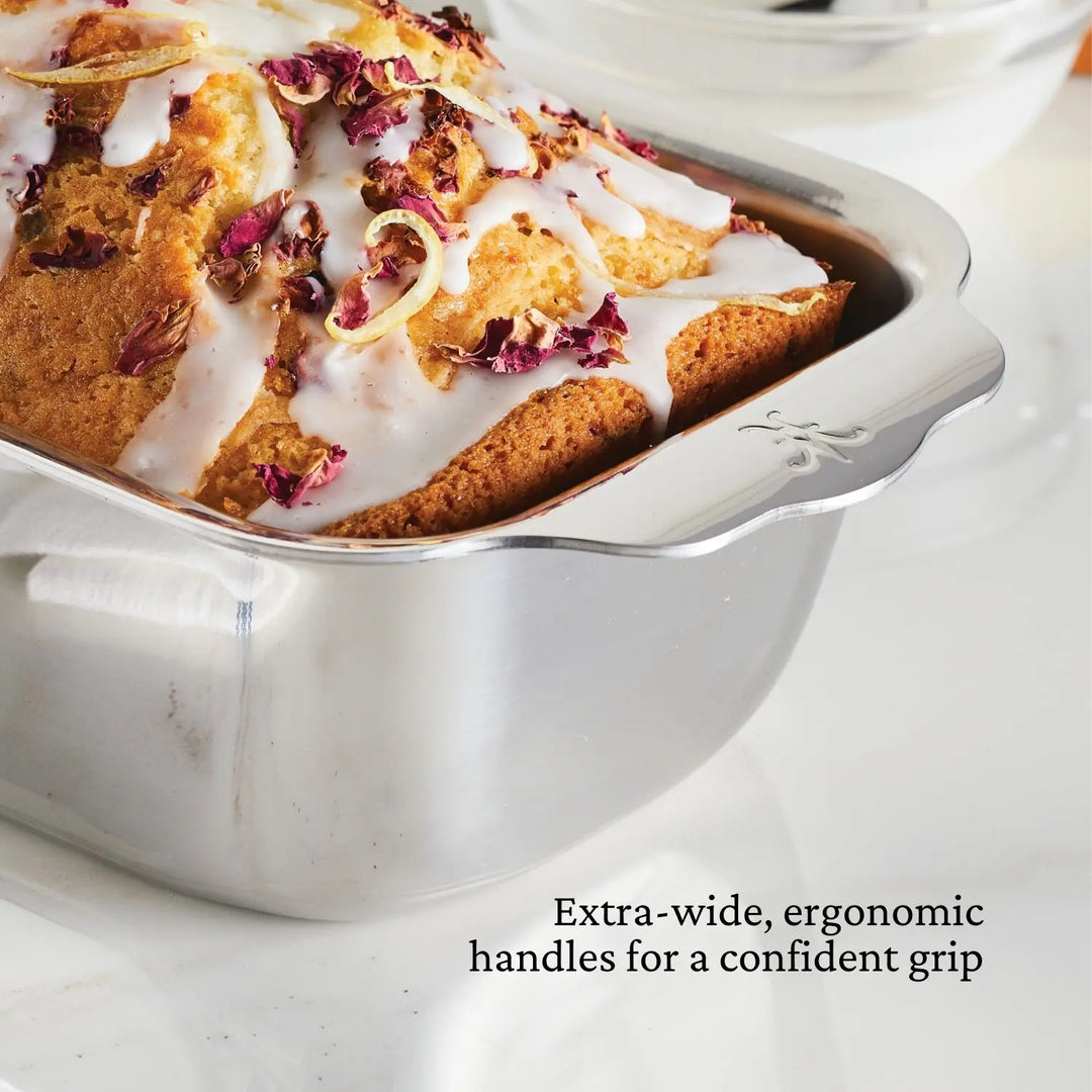 A loaf of iced bread with rose petals in the Hestan Provisions OvenBond Tri-ply Stainless Steel Loaf Pan, featuring extra-wide, ergonomic handles for a confident grip and superior heat conductivity.