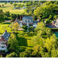 Aerial view of a restored estate from Transformation: Houses, Places, Stories, featuring a brick house, pool, and tennis court set amidst lawns and trees.