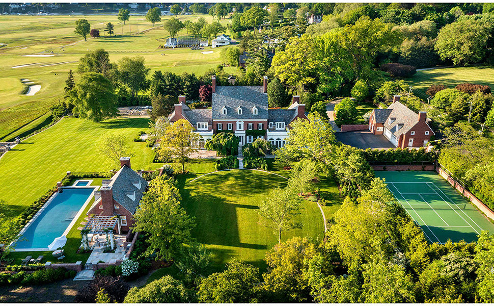 Aerial view of a restored estate from Transformation: Houses, Places, Stories, featuring a brick house, pool, and tennis court set amidst lawns and trees.