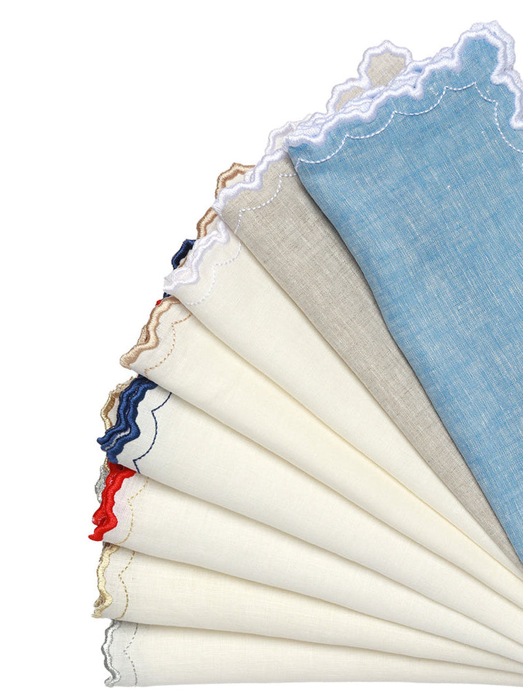 The Kim Seybert Arches Napkin Set features a fanned display of linen napkins in blue, beige, and white, each with delicate embroidered edges—ideal for formal dining.