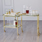 The Global Views Gallery Folding Bar in shiny brass features glass shelves for bottles, glassware, and decanters, set against a light gray wall and wood floor.