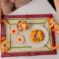 A person holds the Mercedes Salazar Monkey Jungle Party Tray, which is adorned with two bowls of pudding, a plate of cookies, and a plate with a round cake on a white table, creating an inviting dining setting.