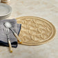 The Cleo Placemat by Blue Pheasant, round and textured in beige with braided edges, sits on a marble surface topped with stacked plates and a folded napkin holding cream-handled spoon and fork.