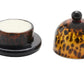 The Blue Pheasant Andrew Tortoise Butter Dish is a durable hand-blown glass set with a tortoiseshell pattern, featuring a round base for butter and a matching dome lid displayed beside it.