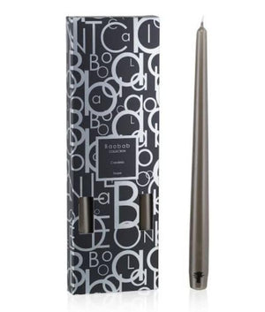 A tall, slender candlestick with a grey glaze stands beside a black and white patterned box labeled "Baobab Collection Candela Candlesticks" by Baobab.