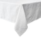A close-up view of the Juliska Berry Scallop Tablecloth from the Berry Scallop Napkin & Tablecloth Collection, featuring its white woven linen draped over the corner of a rectangular table against a white background.