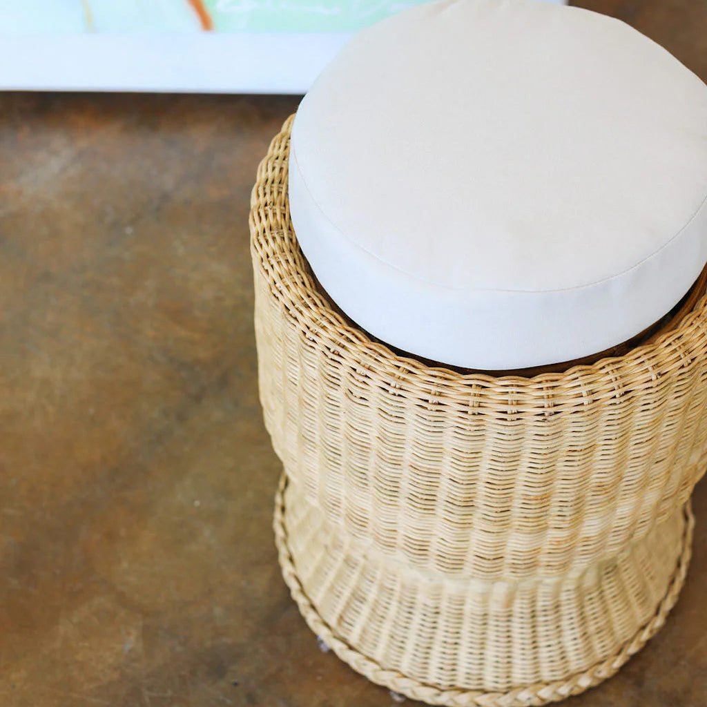 The Varnish Collection Belle Stool features a cylindrical wicker base and a round cream upholstered seat, offering cozy seating. Photographed from above, it's shown on a concrete floor.