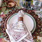 A table setting inspired by the Spanish countryside, featuring a Juliska Seville Stripe Napkin in a wooden ring atop a plate, surrounded by a woven placemat and complemented by a glass of water.