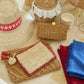 Aerin Bordered Raffia Pouch with a tan center, red border, and two small tassels, resting on a flat woven surface.