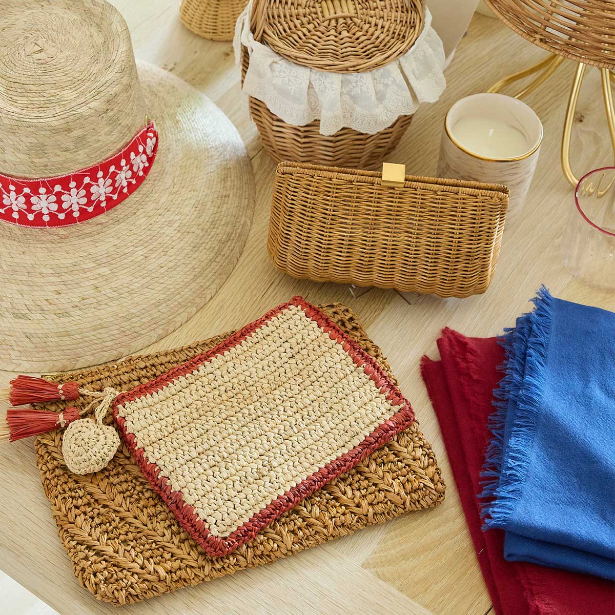 Aerin Bordered Raffia Pouch with a tan center, red border, and two small tassels, resting on a flat woven surface.