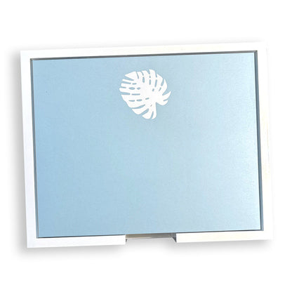 A rectangular light blue card from the Large Blue Note Pad Collection by Black Ink, featuring a white monstera leaf at the top center and a white border.