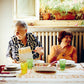 Four elderly women sit around a table in a sunlit kitchen adorned with potted plants on the windowsill, sharing laughter and heartfelt stories as they prepare delicious meals inspired by Pasta Grannies: Comfort Cooking from Chronicle Books.
