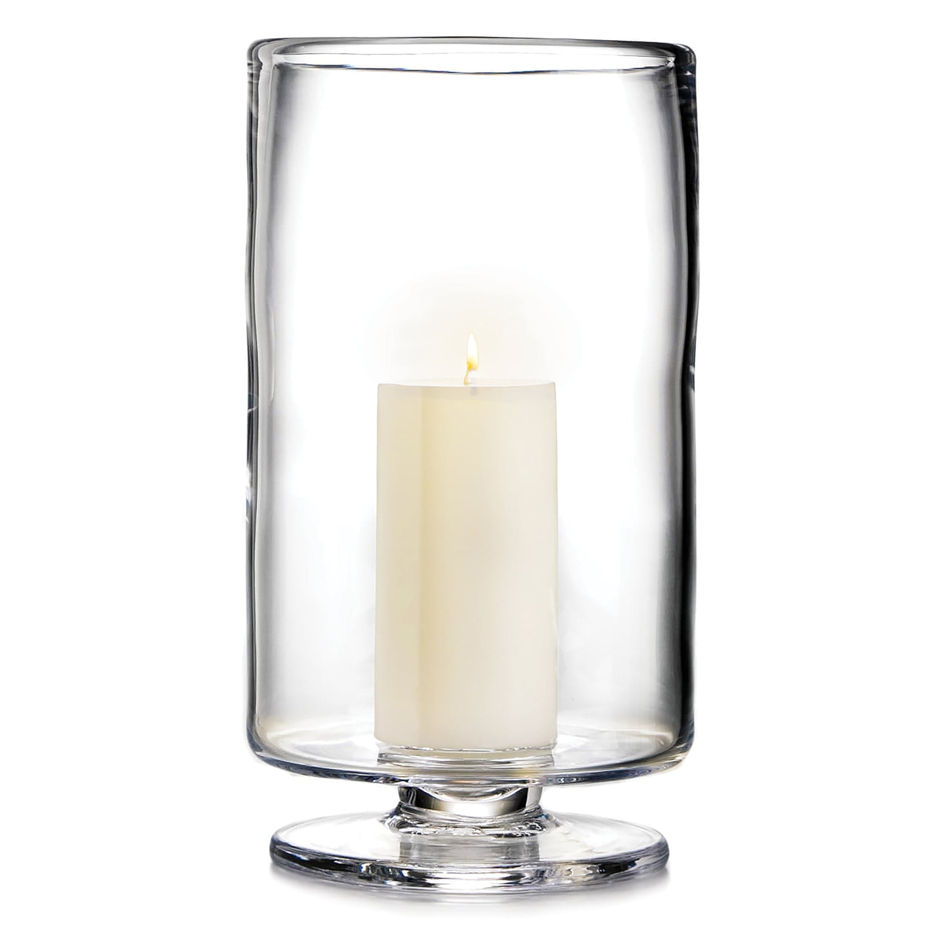 A white pillar candle glows inside a tall, clear Simon Pearce Nantucket Hurricane Collection candle holder with a wide base.
