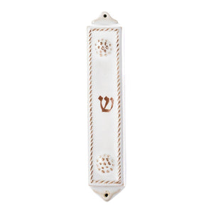 The Juliska Berry & Thread Whitewash Mezuzah is a white ceramic case with Berry & Thread detailing, a central brown "Shin," and wall-mounting holes at the top and bottom.