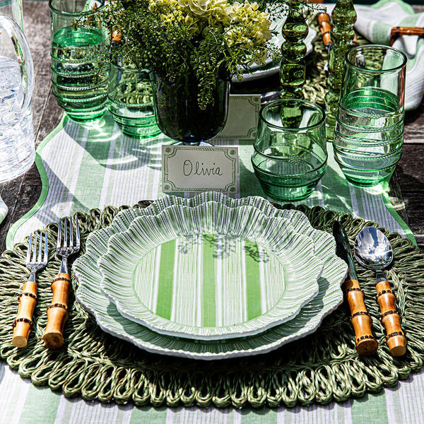 Table setting with Juliska-inspired green and white striped plates, bamboo-handled cutlery, green glasses, a floral centerpiece, and Berry & Thread Place Cards by Juliska labeled "Olivia.