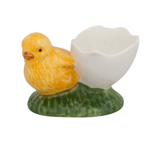 The Bordallo Pinheiro Egg Cup with Chick by Bordallo Pinheiro showcases a yellow chick beside a white eggshell on a vibrant green base, ideal for enhancing your spring table decor.