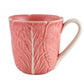 The Pink Cabbage Leaf Dinnerware and Serveware Collection by Hive features a pink ceramic mug with a handle, adorned with a leaf-textured pattern inspired by Raphael Bordallo Pinheiro’s iconic designs.