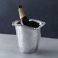 A bottle of Moët champagne rests in a Beatriz Ball Organic Pearl Ice Bucket Collection piece, featuring a wavy beaded rim, on a gray surface against a dark background.