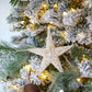 A close-up of a decorated Christmas tree with frosted branches, warm lights, the Dekorasyon Mini Pearl Bottlebrush Star Ornament, and a round white bauble.