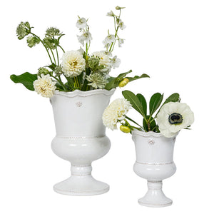 Two white vases from the Juliska Berry & Thread Petite Parterre Whitewash Garden Vase Collection, featuring a whitewash glaze and scalloped edges, are filled with elegant white and green flowers and fresh green leaves.
