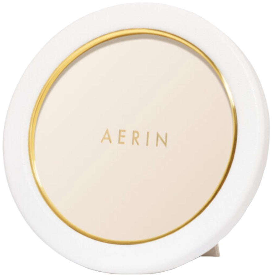 The Aerin Piero Leather Frame Collection features a round photo frame with white and gold detailing, crafted from Italian leather for an elegant display. The brand name "AERIN" appears at the center.