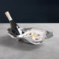 The Beatriz Ball Ocean Oyster Champagne Bucket Collection elegantly displays a bottle of champagne and three oysters on ice with a lemon wedge, all arranged on a gray surface.