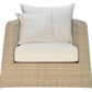 The Janus et Cie Zeya Outdoor Lounge Chair is a beige wicker armchair with weather-resistant white seat and back cushions, plus two square white pillows—ideal for outdoor living and shown from the front.
