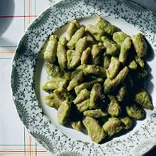 A decorative plate filled with green gnocchi, inspired by the recipes in *Pasta Grannies: Comfort Cooking* from Chronicle Books, sits on a white tablecloth with a faint plaid pattern.