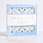 The WS Game Company's Scrabble Bianco Edition features a deluxe rotating board with a wood frame and premium components, elegantly displayed on a light surface.