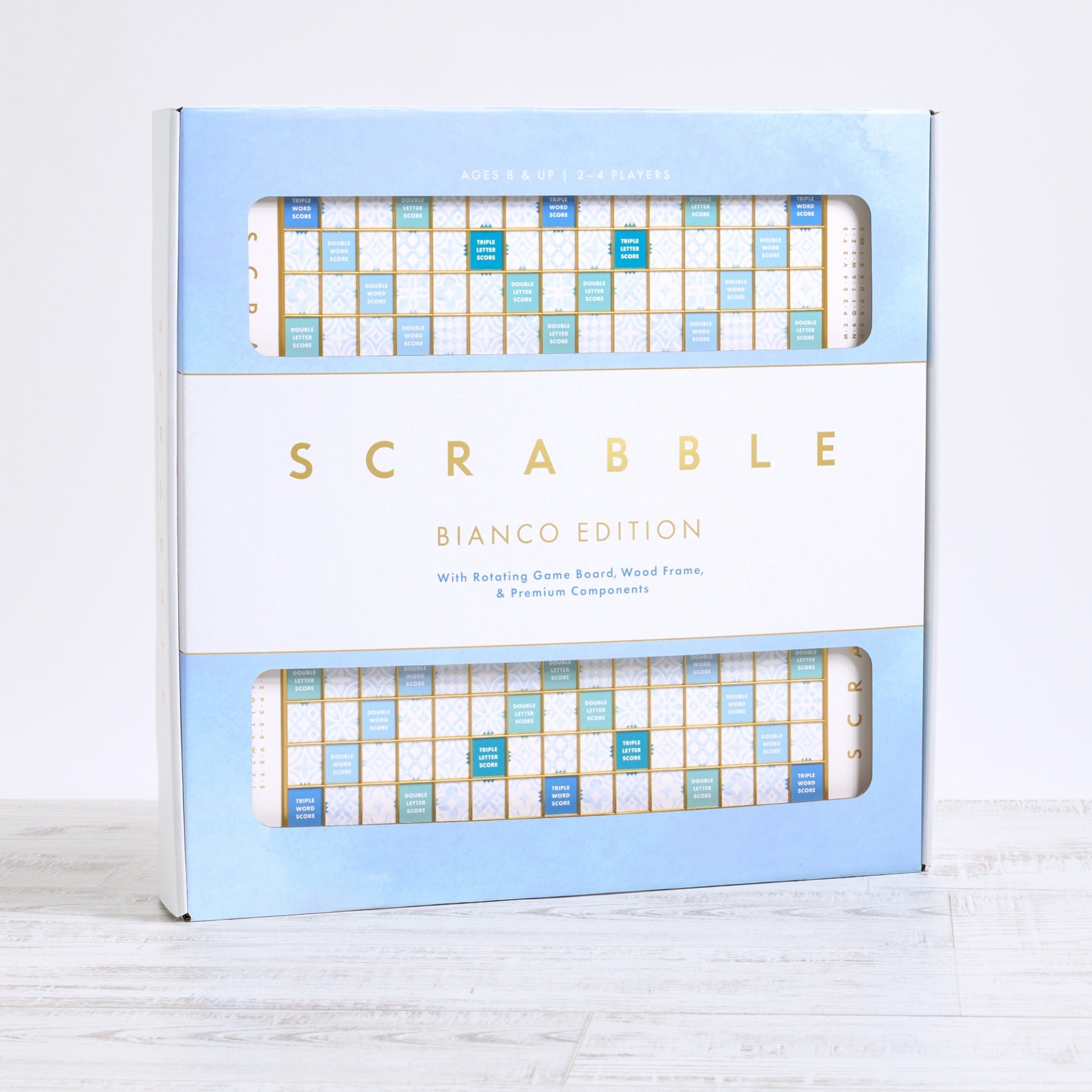 The WS Game Company's Scrabble Bianco Edition features a deluxe rotating board with a wood frame and premium components, elegantly displayed on a light surface.