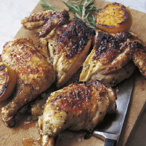 Quartered roast chicken arranged on a wooden board, accompanied by grilled lemon halves and fresh rosemary sprigs—a simple yet flavorful home-cooked meal inspired by *Barefoot Contessa Back To Basics* from Penguin Random House.