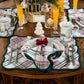 A festive table features plaid placemats, Berry & Thread holiday plates and mugs, silverware, napkins tied with red bows, orange drinks, and a “Sarah” place card in Juliska’s Berry & Thread White Tree Place Card Holder Set.